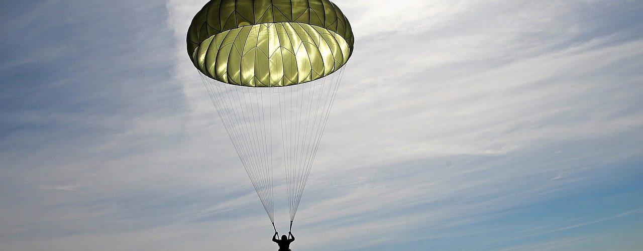 Fallskärmshoppare med grön fallskärm landar säkert på marken.