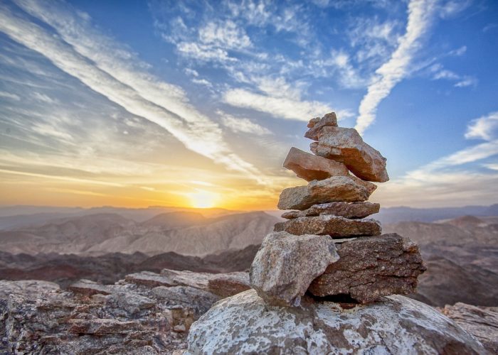 Ett tiotal stenar balanserar på varandra. Solnedgång över bergen i bakgrunden.