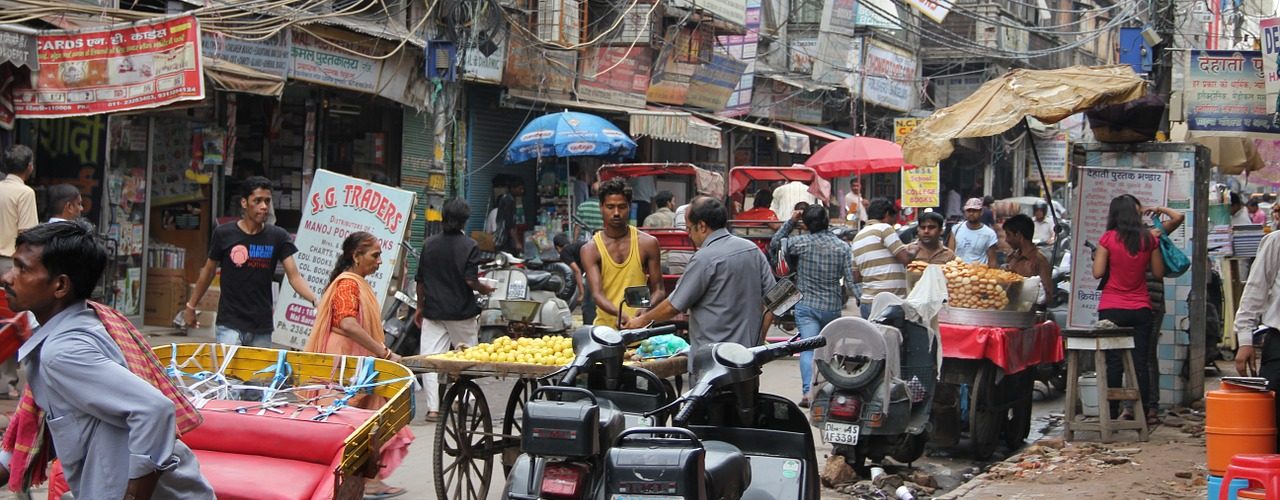 Bild från New Dehli med många bilar, stånd och elledningar som hänger från husen. Kaotiskt.