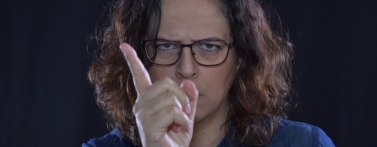 Argsint kvinna med permanentat brunt hår. Hon rynkar ögonbrynen och hytter med fingret.