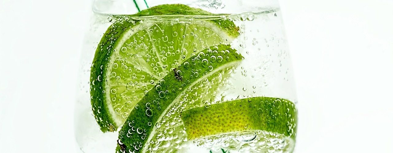 Ett glas med bubblig dryck, tre gröna limeskivor och en drinkpinne.