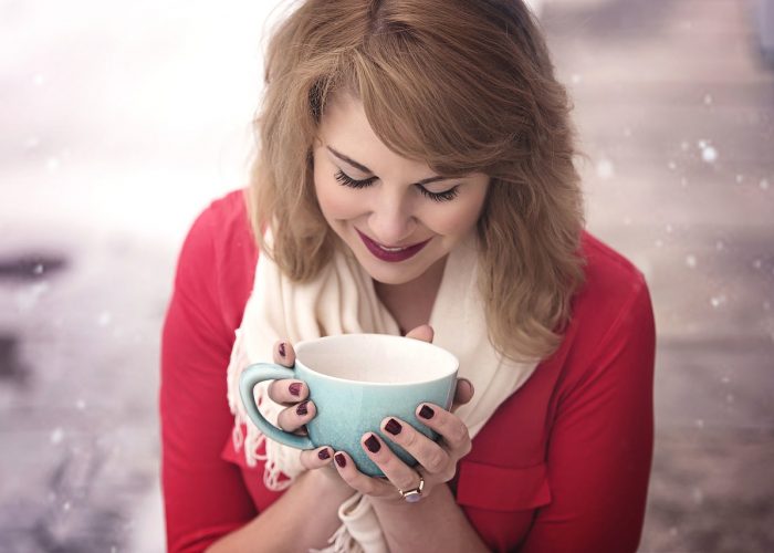 Kvinna med röda läppar coh röd tröja som lyckligt håller i en turkos kaffekopp.